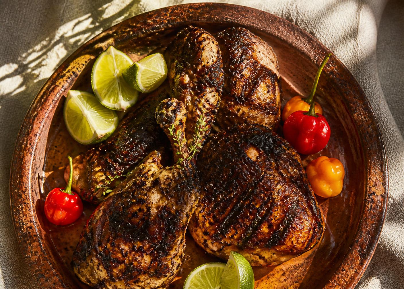 Charred jerk chicken on a clay platter with lime and scotch bonnet peppers